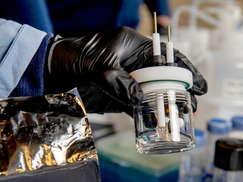 A gloved hand holding one of the test cells that looks like a small glass jar.