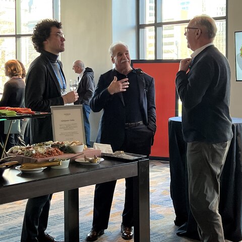 Three people stand near a table talking.