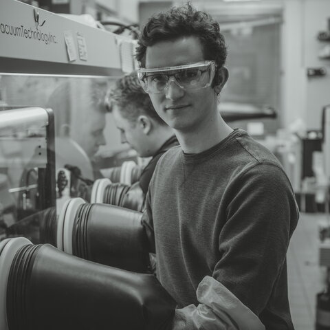 Black and white photo of Daniel Szczepankiewicz in the lab with his arms in a glove box.