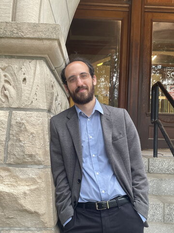 Paul Griffin with hands in pant pockets, stands leaning against one side of arched entrance to Noyes. 