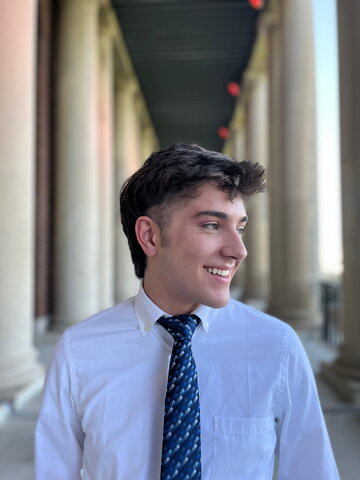 Portrait of Joel Ryan standing outdoors with head turned to the side and large pillars in the background