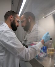 Matthew Boudreau in a white lab coat and blue rubber gloves working in the lab