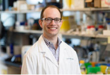 Portrait of Dan Heller in a white lab coat in a lab setting