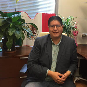 Professor Joaquín Rodríguez-López sitting in his office in front of a Mexican flag