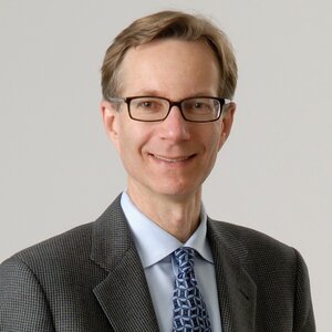 Head shot of Steve Zimmerman in a suit jacket, white shirt and blue tie on a gray background