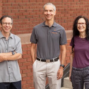 The three researchers standing side by side outdoors in front of a brick wall.