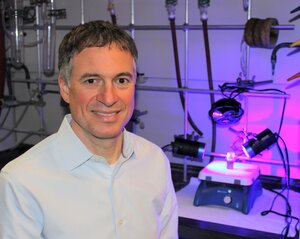 Photo of Liviu Mirica sitting next to lab equipment.