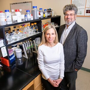 Jonathan Sweedler stands next to Marni Boppart near a counter in the lab with shelves of bottles and other lab equipment behind them.