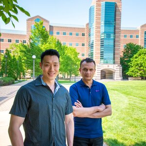 Jeff Chan, left, stands outdoors on the engineering quad on the UIUC campus and side by side with Anuj Yadav, with arms folded; the Beckman Institute is in the background. 