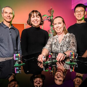 Four-member team of chemists pictured side by side behind a lab table with kit pieces in front of them.