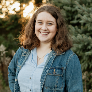 Outdoor portrait of Katie standing in front of trees with sun shining through trees.