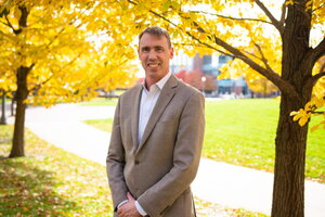 Portrait of Paul Hergenrother standing outdoors with yellow fall colored trees and a pathyway in the background.