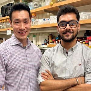 Jeff Chan and Suritra Bandyopadhyay stand side by side in a lab with shelves lab supplies in background