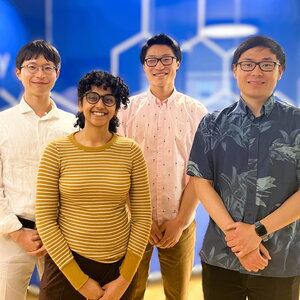 Four researchers stand side by side in front of a blue wall with molecular illustrations