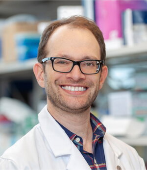 Portrait of Dan Heller in white lab coat in a lab setting