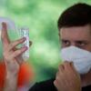 Photo of a student with a mask looking at a saliva sample test tube