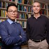 Image of Martin Gruebele, right, and graduate student Huy Nguyen, left, standing next to each other in front of a wall of bookshelves filled with books.