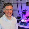 Photo of Liviu Mirica sitting next to lab equipment.