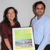 Professor Prashant Jain, right, stands holding a framed event poster with Rice University professor Naomi Halas, left, who's also standing holding the poster.