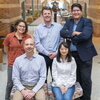 Five members of the research team two seated and three standing pose together in the atrium of the Beckman Institute.