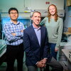 Three members of the research team pose together, two standing and Hergenrother seated, in a lab on campus.