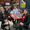 A group of event attendees sitting in chairs at a table in an outdoor venue